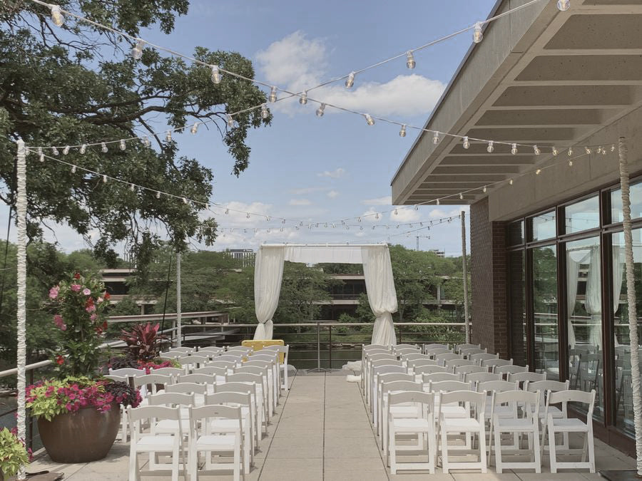 A patio with white chairs and a canopy, featuring Italian String/Market lighting and providing an outdoor ceremony space.