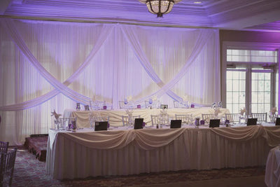 The elegant wedding ceremony site features a long table with a white cloth, creating an exquisite fabric backdrop with purple uplighting for reception photos.