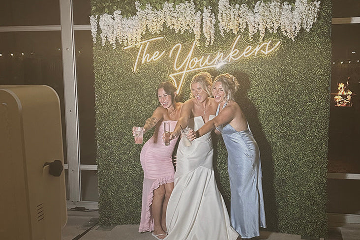 Three women posing in front of a decorative backdrop with 'The Younkers' neon sign.