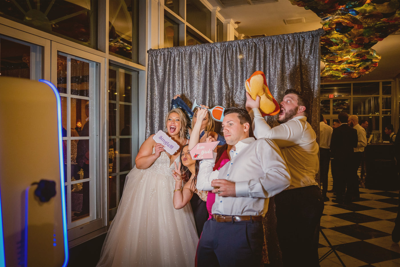 A bride and groom strike a funny pose with friends in a magic mirror style photo booth with a deluxe backdrop.