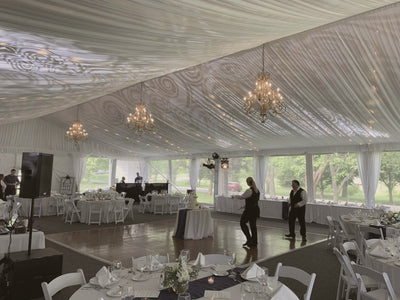 A wedding reception tent with beautiful white ceiling draping lit by multiple ornate chanedliers