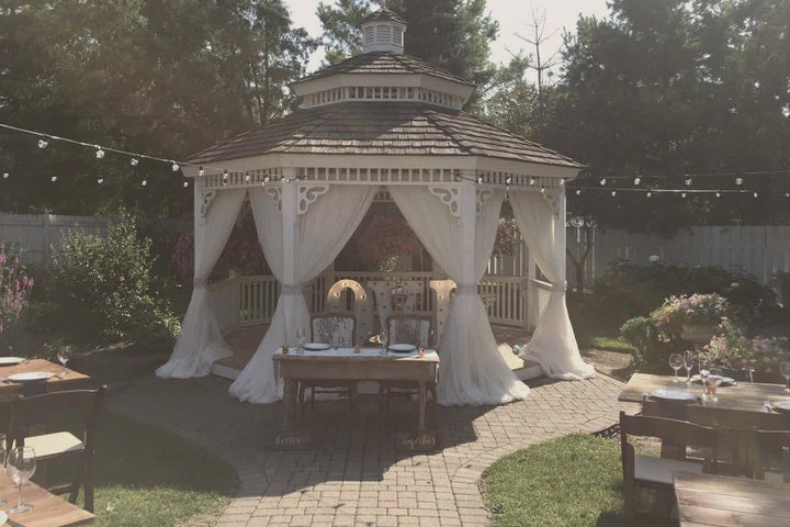 A gazebo with clean white draped fabric in a backyard.