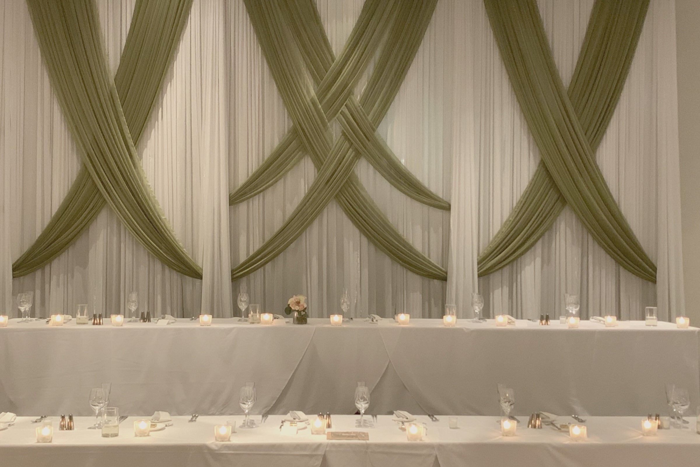 White fabric draped wall with sage green crossed fabric draped over the white