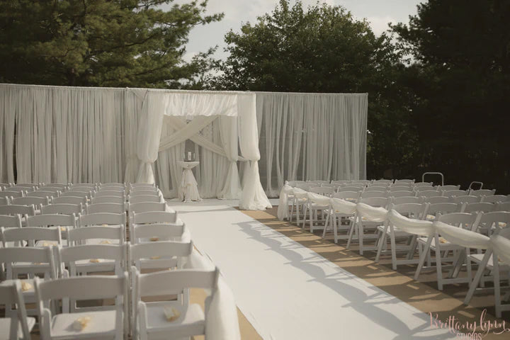 An outdoor wedding ceremony set up with draped white chairs and a white chuppah.