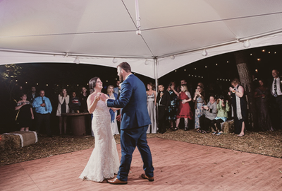 A bride and groom gracefully share their first dance under a tent, surrounded by delighted guests at their wedding venue.