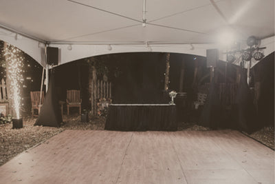 A tented wedding reception area ready for a party with a large dance floor, DJ booth, lighting, and cold sparks