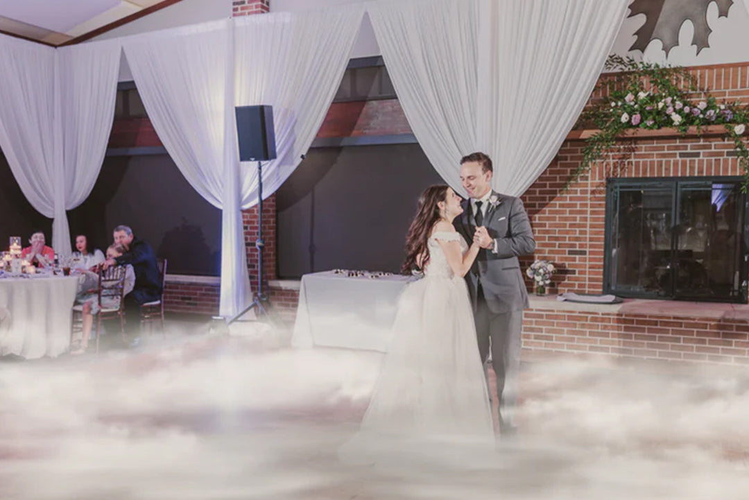 A magical dance floor fog effect transforms a reception space into an enchanting setting as a man and woman gracefully share their first dance. 