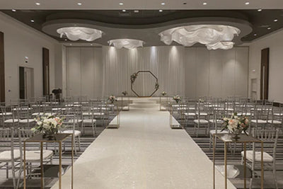 A large room transformed into a stunning wedding venue, adorned with beautiful decor and set up for the arrival of guests. The focal point of the room is a grand stage where the wedding couple will exchange their vows.