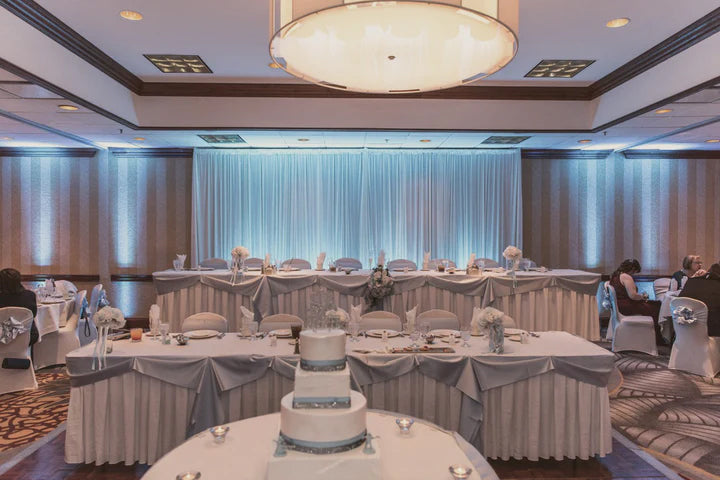 A wedding reception set up in a hotel ballroom venue, featuring pale blue room uplighting.